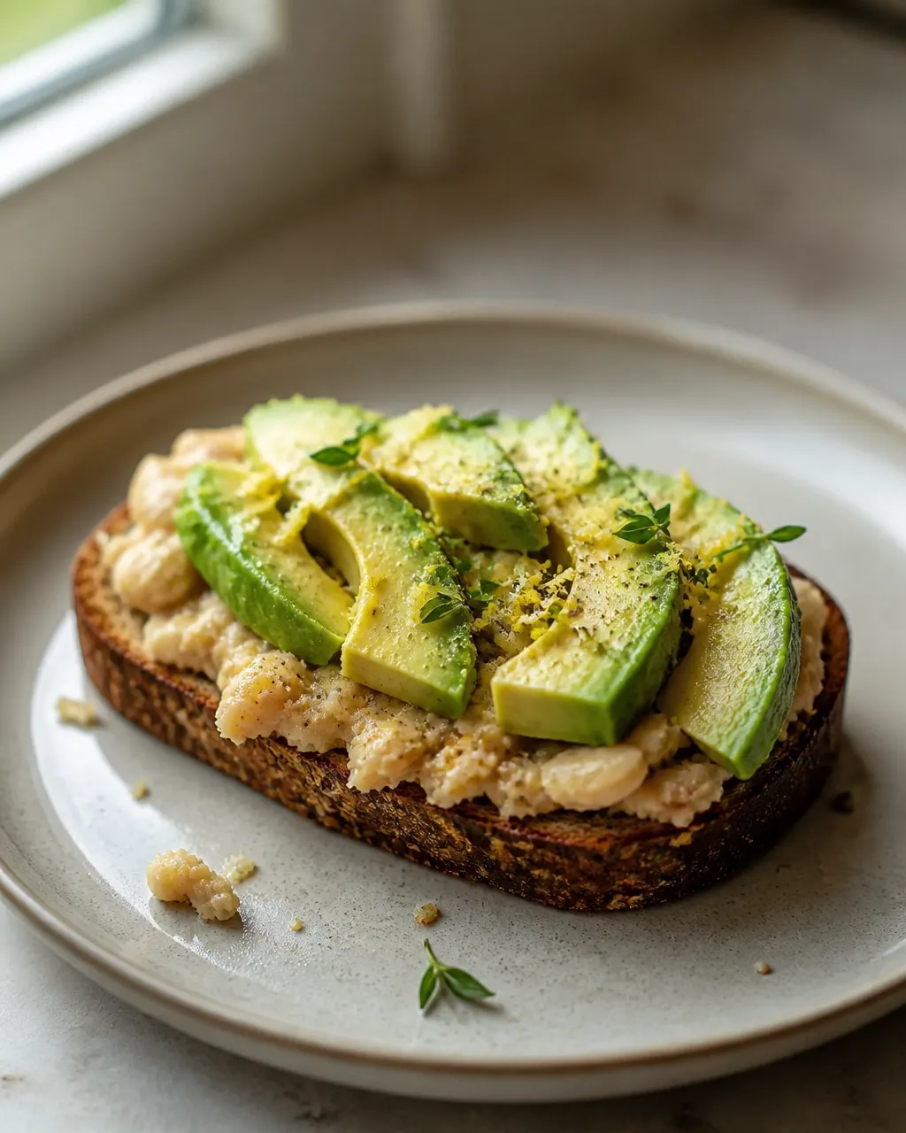 Rustic avocado and white bean toast with lemon zest, herbs, pepper, and natural crumbs